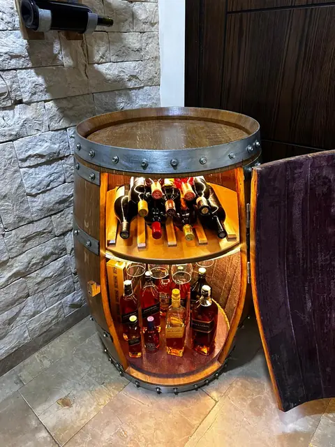 The barrel bar standing open and lit from inside, bottles on both shelves.