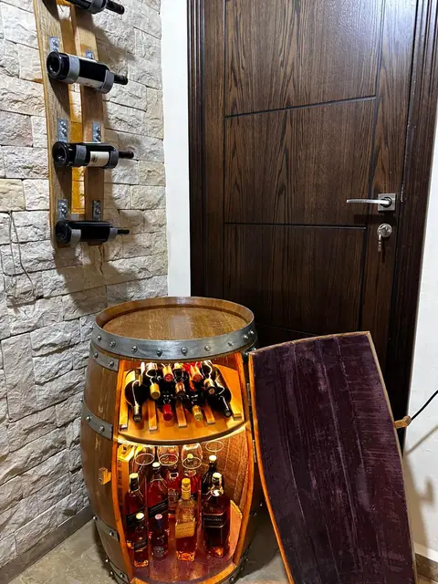 A barrel bar open against a stone wall, its interior lit warm, bottles on both shelves.