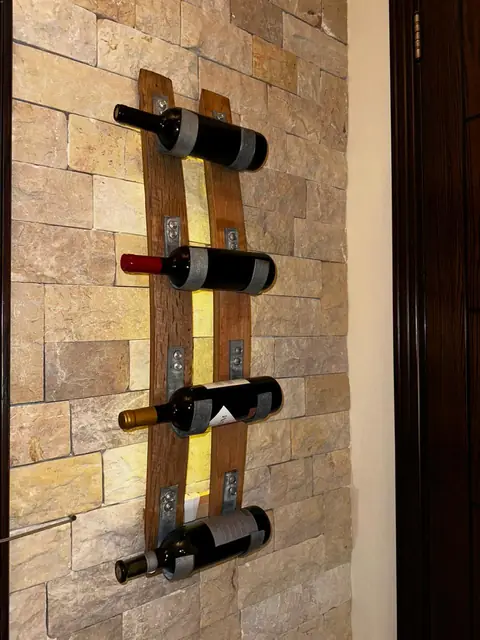 A backlit oak wall rack holding four bottles on a stone wall.